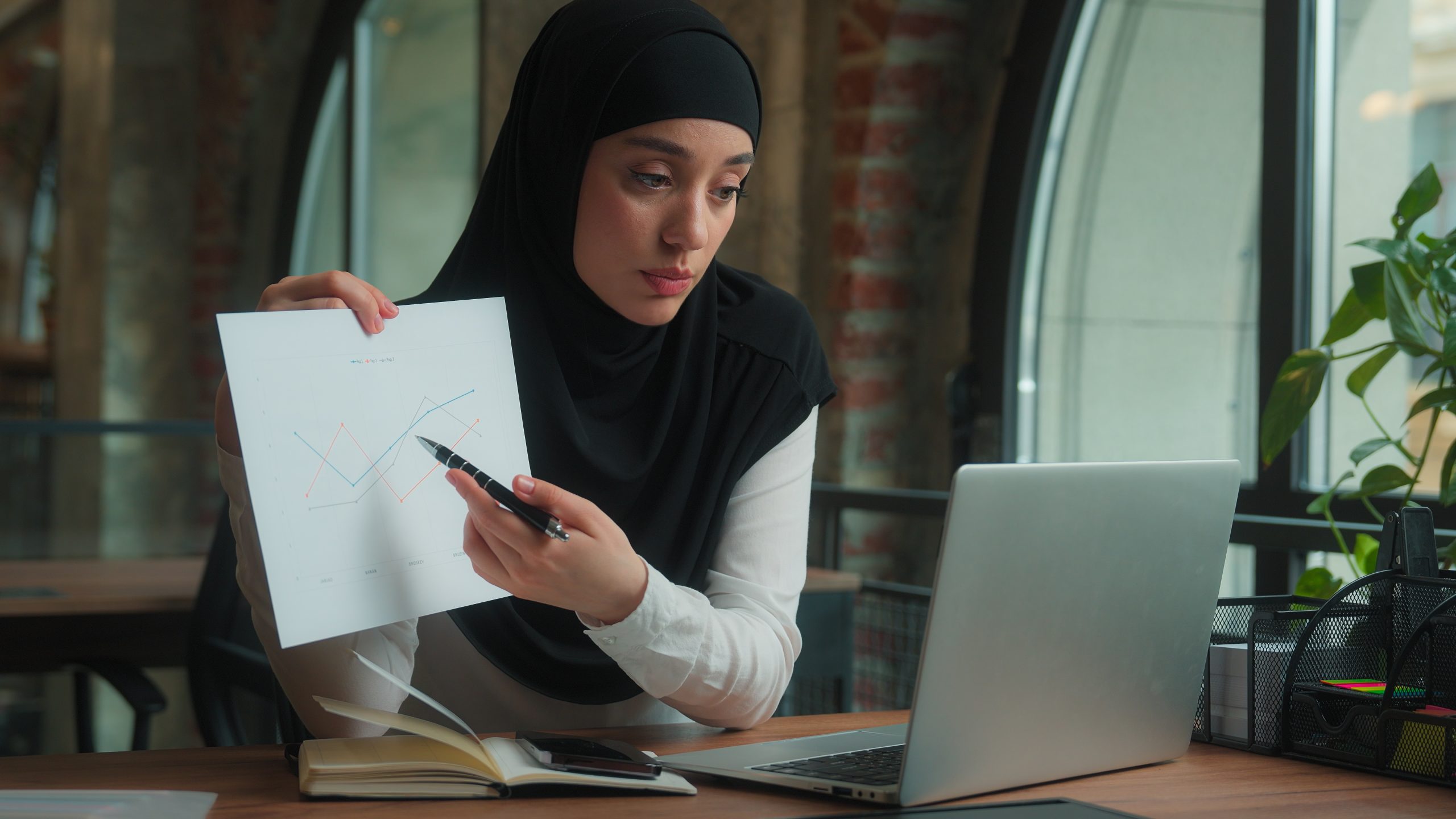 Muslim Arabian islamic girl in hijab smiling woman female businesswoman saleswoman laptop video call online confrence pointing on paper document discuss report sales graph business presentation office. High quality 4k footage